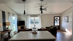 A spacious kitchen with a central island, pendant lights, ceiling fans, and a large window with curtains.