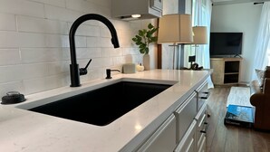 A modern kitchen with a black sink, white cabinets, and a marble countertop.