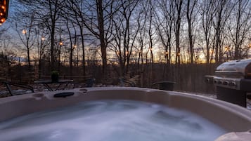 Relax in a serene hot tub surrounded by a forest view and outdoor seating area with a grill.