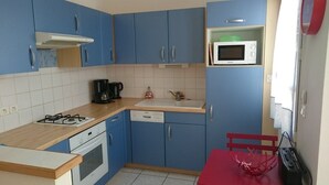 Una cocina compacta con armarios azules, un microondas, una estufa a gas, una cafetera y una silla roja.