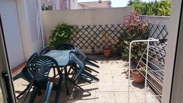 Un patio con una mesa, sillas, una planta en maceta y una reja de metal.