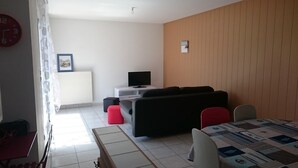 Una sala de estar con un sofá, un televisor, un radiador y una mesa de comedor con sillas.