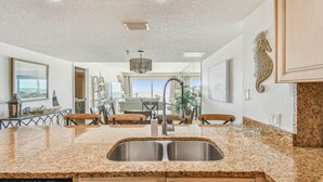 Una cocina con encimeras de granito, pileta de acero inoxidable, armarios de madera y una decoración de caballito de mar en la pared.