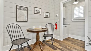 A dining area with a round wooden table, two metal chairs, and framed artwork on the wall. - The Cottages at Laurel Brooke (Peachtree City)