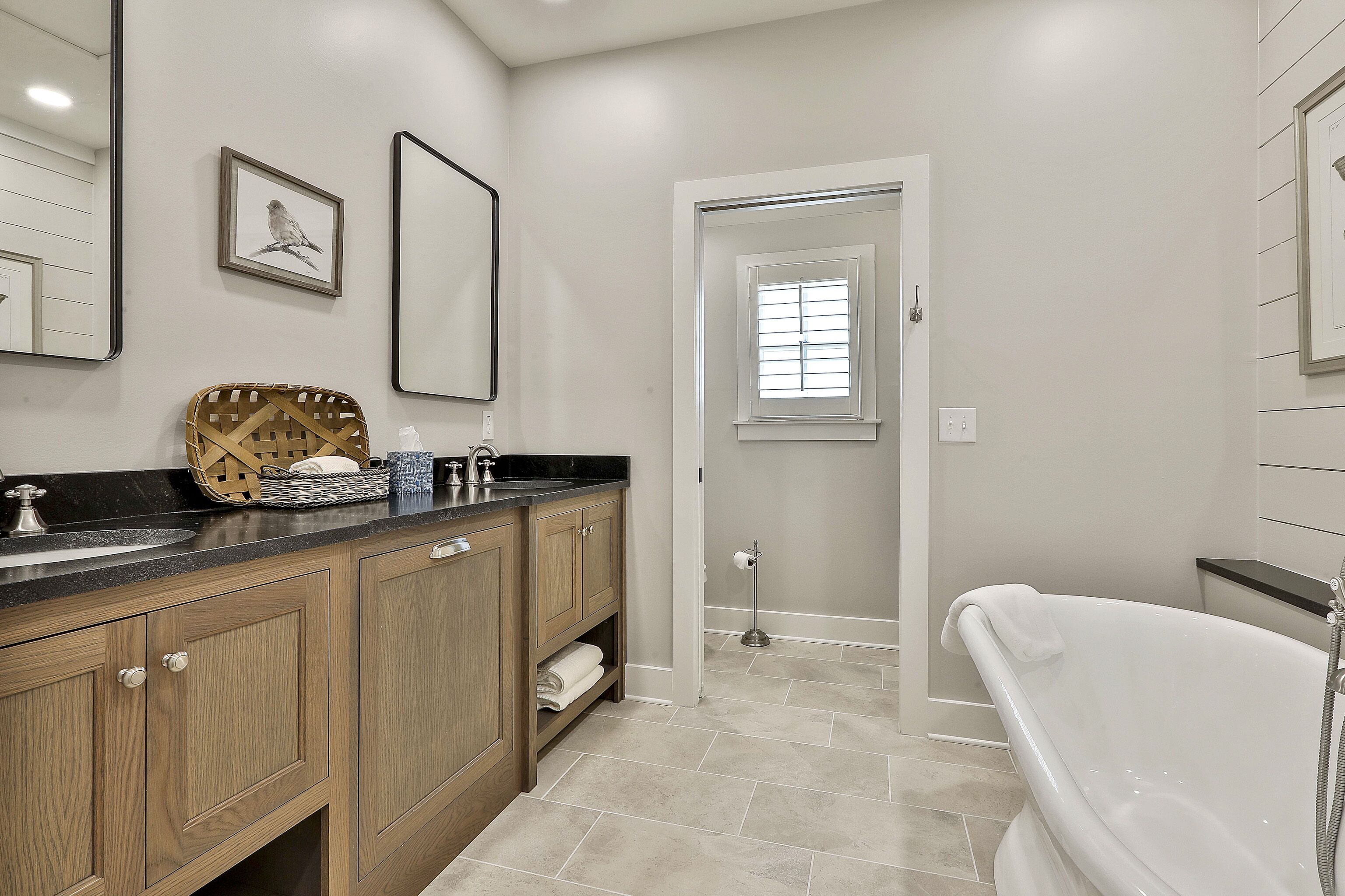 A modern bathroom with a wooden vanity, a white bathtub, and a window providing natural light.