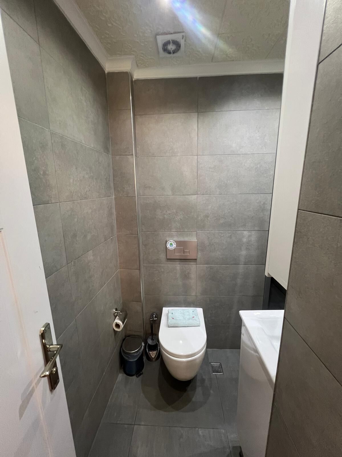 A small, modern bathroom with grey tiles, a toilet, a bidet, and a trash bin.