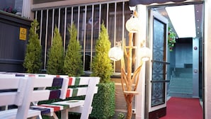 An outdoor seating area with white benches, a decorative wooden structure with hanging lights, and neatly trimmed bushes. -  Middle Village (Istanbul)