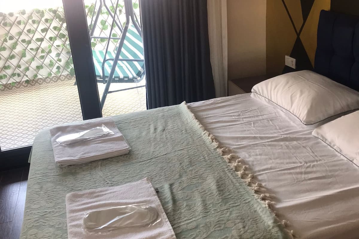 A hotel room with a bed, a window with curtains, a view of the outside, and a patterned bedspread.