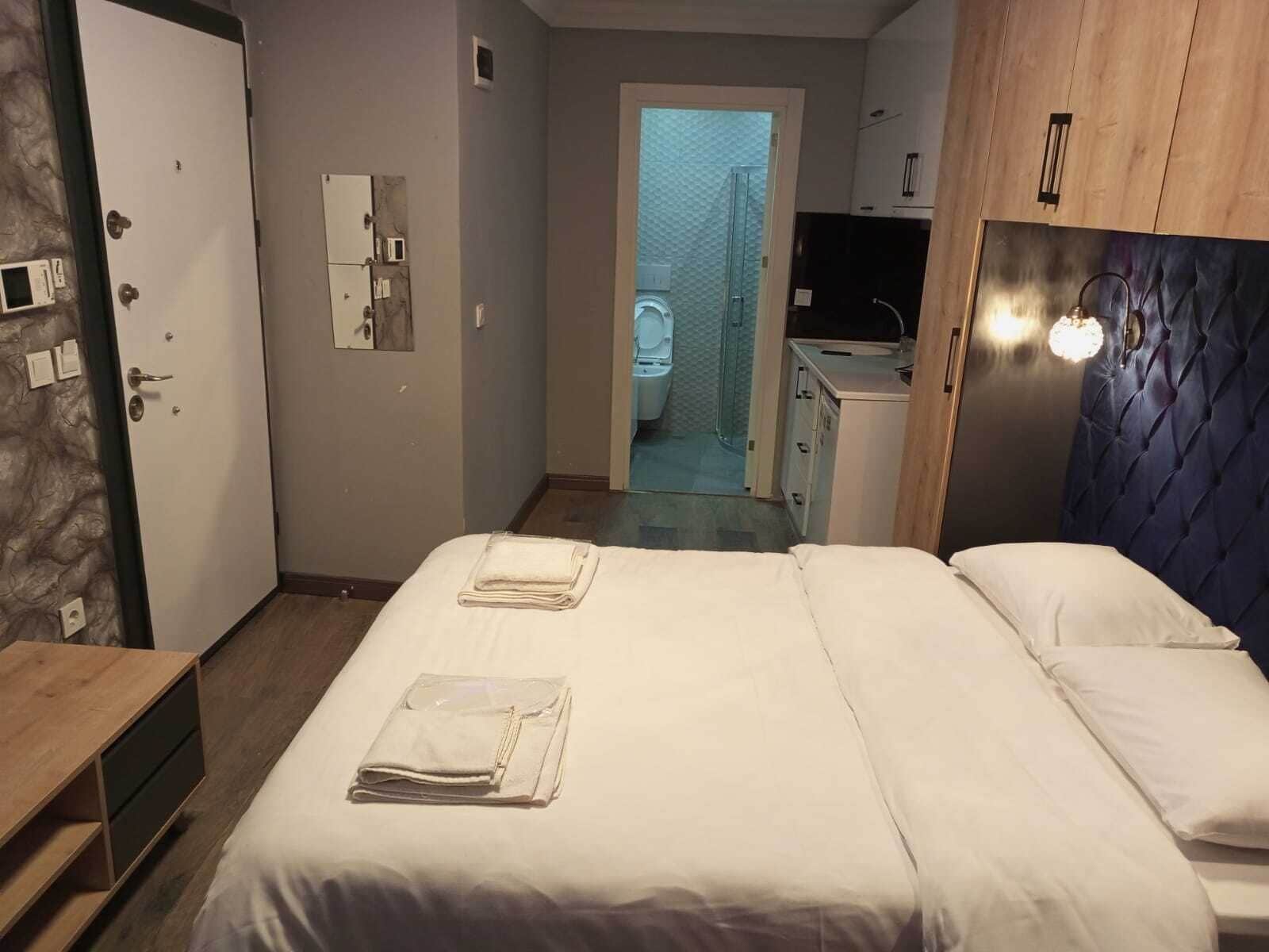 A hotel room with a bed, a desk, a wardrobe, and a bathroom visible through an open door.