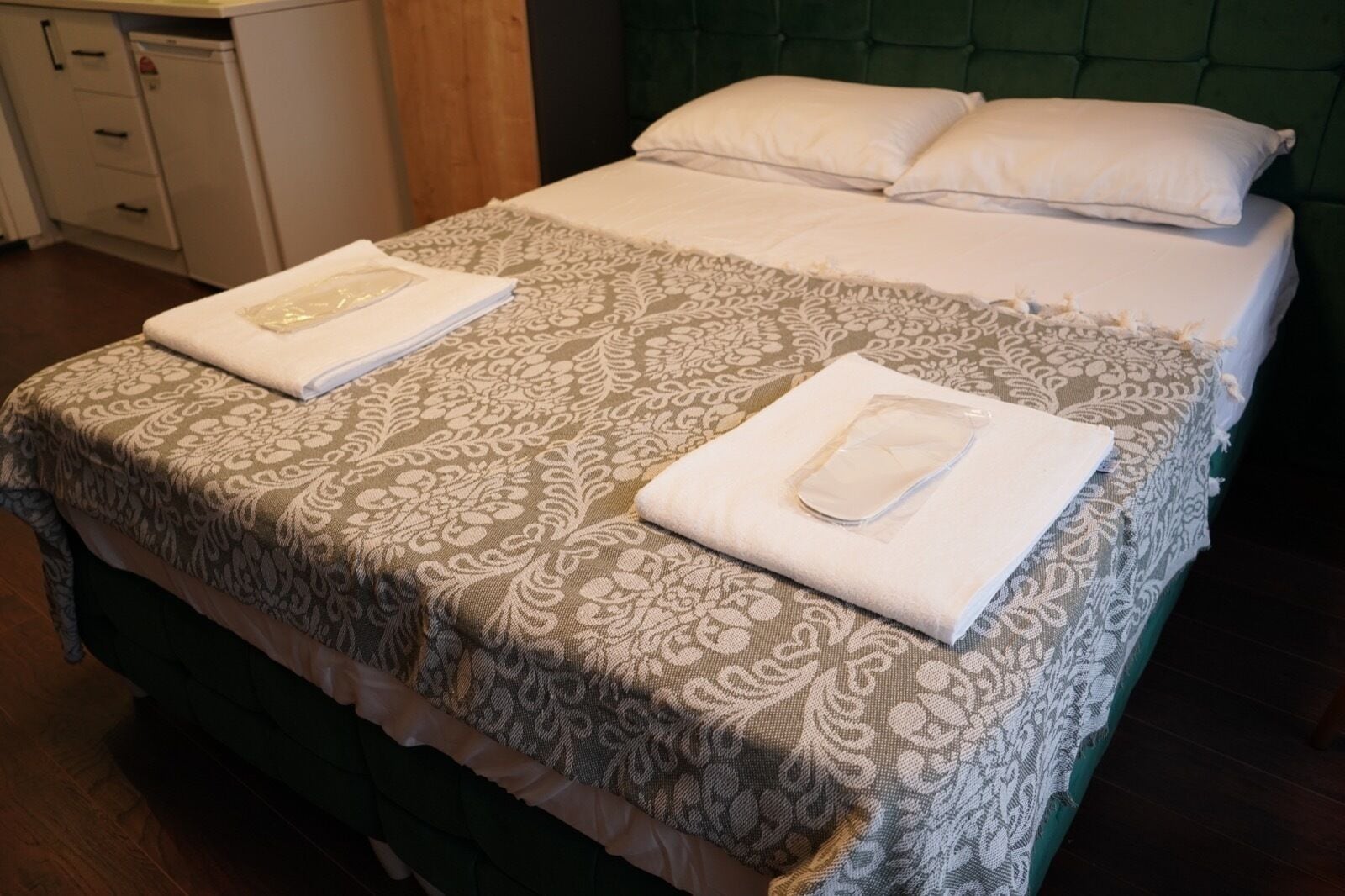 A neatly made bed with a patterned bedspread and two towels folded on top.