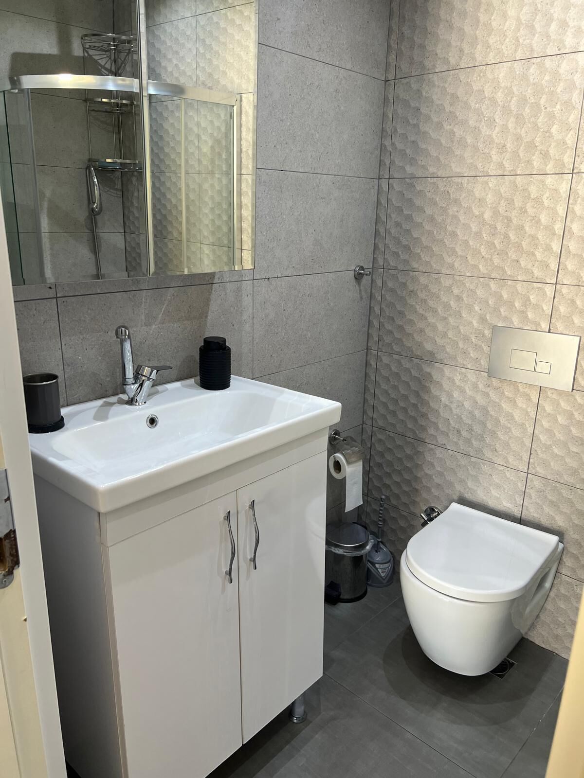 A bathroom with a white sink, a mirror, a toilet, and a shower area.