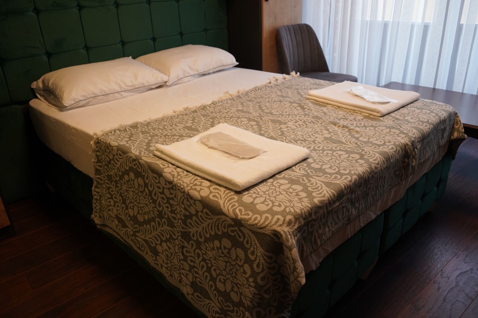 A neatly made bed with a green headboard, a patterned bedspread, and two folded towels on the bed.