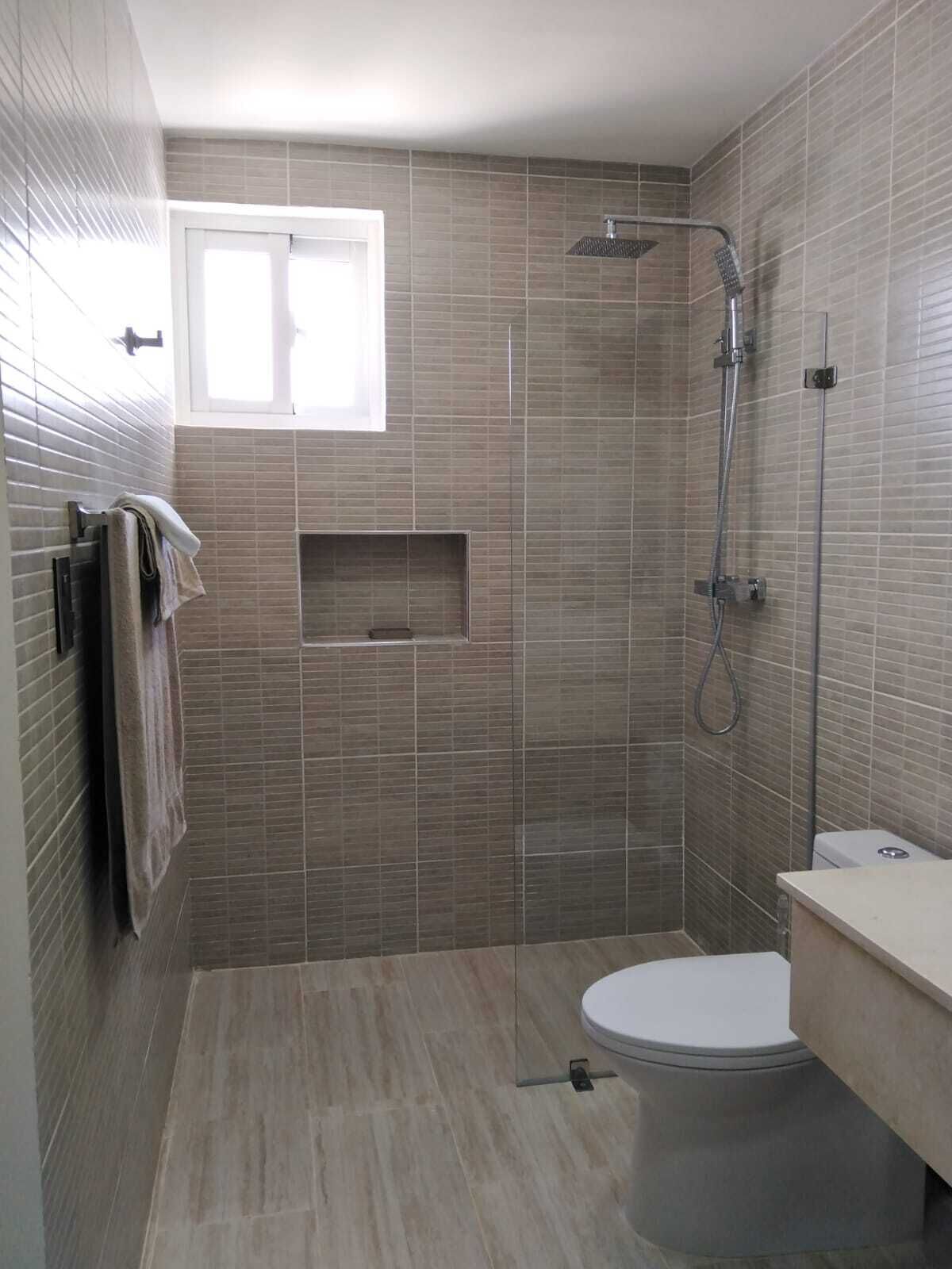 A modern bathroom with a shower, toilet, and a small window.