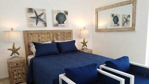 Un dormitorio con cabecera de madera, una cama grande con ropa de cama azul, dos mesitas de noche con lámparas en forma de estrella de mar y un espejo en la pared.