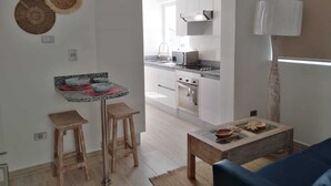 Una cocina moderna con armarios blancos, horno empotrado y microondas. Cuenta con un comedor con una mesa pequeña y dos taburetes.