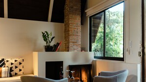 Una sala de estar moderna con chimenea, dos sillones, una mesa de centro y un ventanal con vistas a zonas verdes.