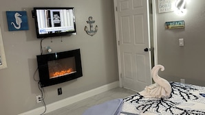 Ein Schlafzimmer mit Bett, einem an der Wand befestigten Fernseher, einem Kamin und einer Tür.