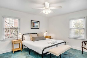 Un dormitorio con cama, mesitas de noche, un banco y un ventilador de techo.
