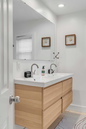 Un baño moderno con un tocador blanco, dos lavamanos, un espejo grande y armarios de madera.