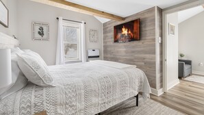 Un dormitorio moderno con chimenea, una cama con colcha estampada y vistas al exterior a través de una ventana.