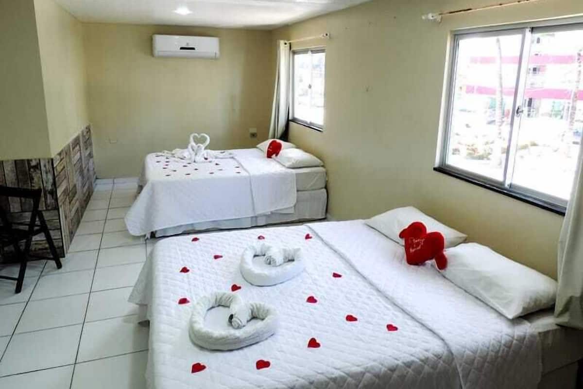 Ein Hotelzimmer mit zwei Betten, jedes mit herzförmigen Bademänteln und Rosenblättern.