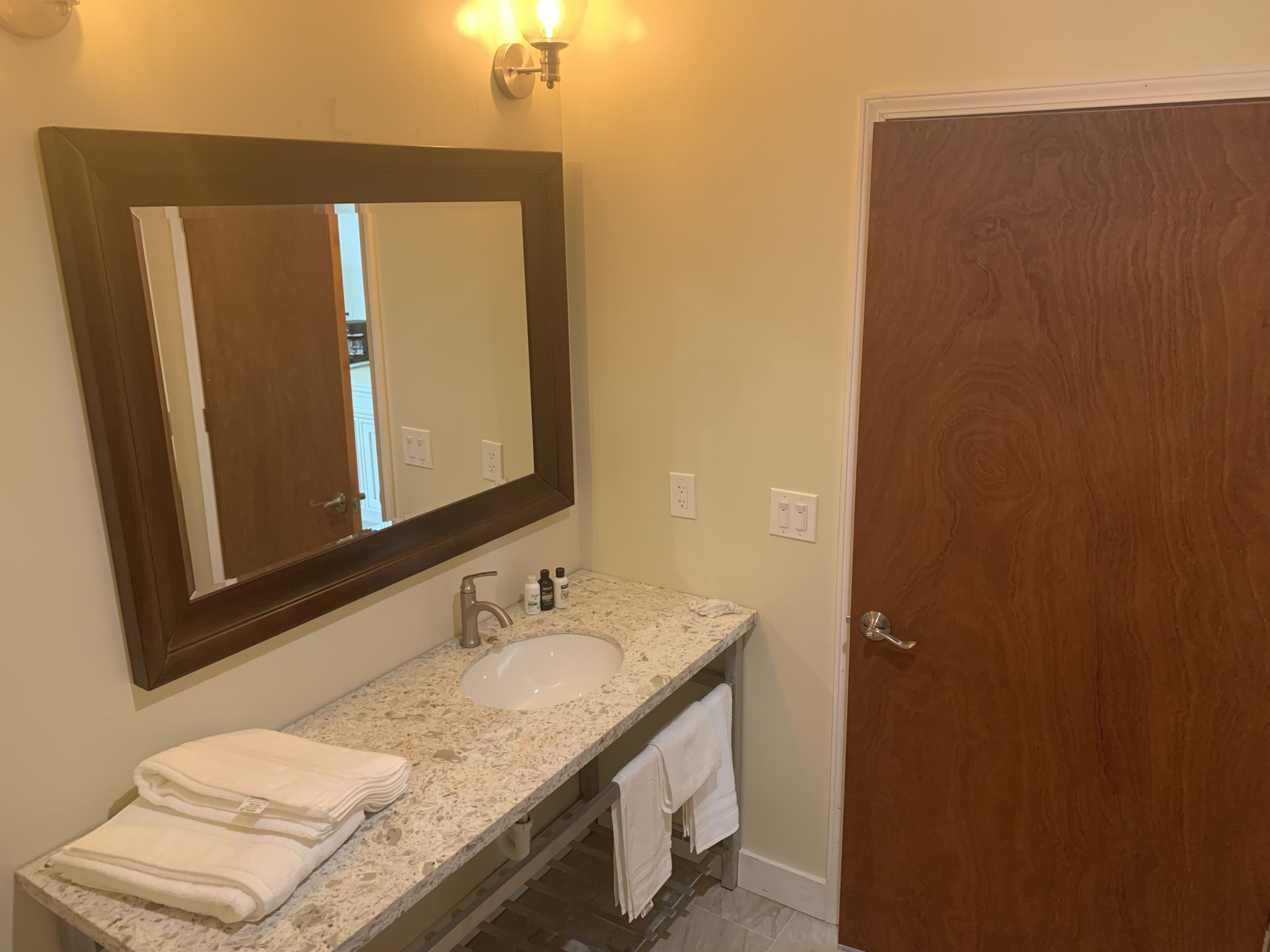 A bathroom with a marble sink, a large mirror, and a wooden door.