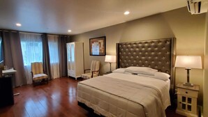 Une chambre d’hôtel avec un grand lit, une chaise, un bureau, une armoire et un tableau au mur.