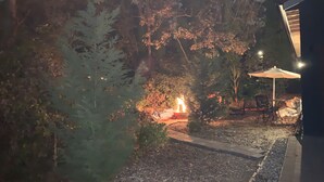 Un espace jardin aménagé avec un foyer, entouré d’arbres et bordé d’un sentier.
