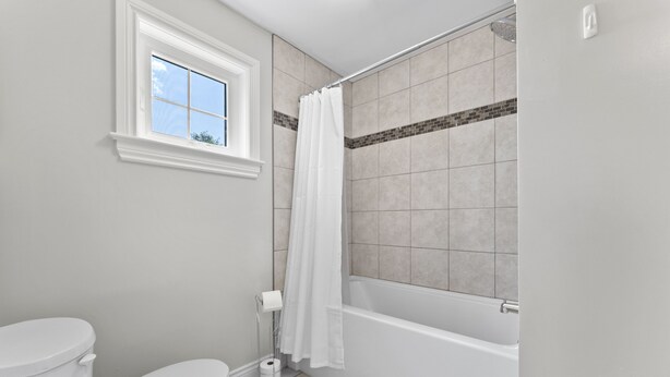 Ein Badezimmer mit Toilette, Fenster, Dusche mit Vorhang und Badewanne.