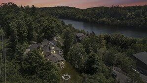 Ilmakuva asuinalueesta, jossa on useita taloja, ja aluetta ympäröi tiheä metsä, järvi ja tie.