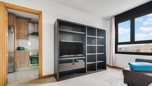 A modern apartment with a kitchen, a large black entertainment unit, and a window with a city view.