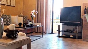Una sala de estar con televisor, una mesa de centro, un jarrón con flores y un sofá.