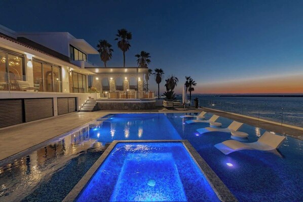 Un espace piscine moderne offrant une vue sur le coucher de soleil, un coin salon abrité et des palmiers.