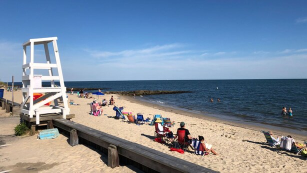 En strand med en livredderstand, strandstole og mennesker, der nyder sand og vand.