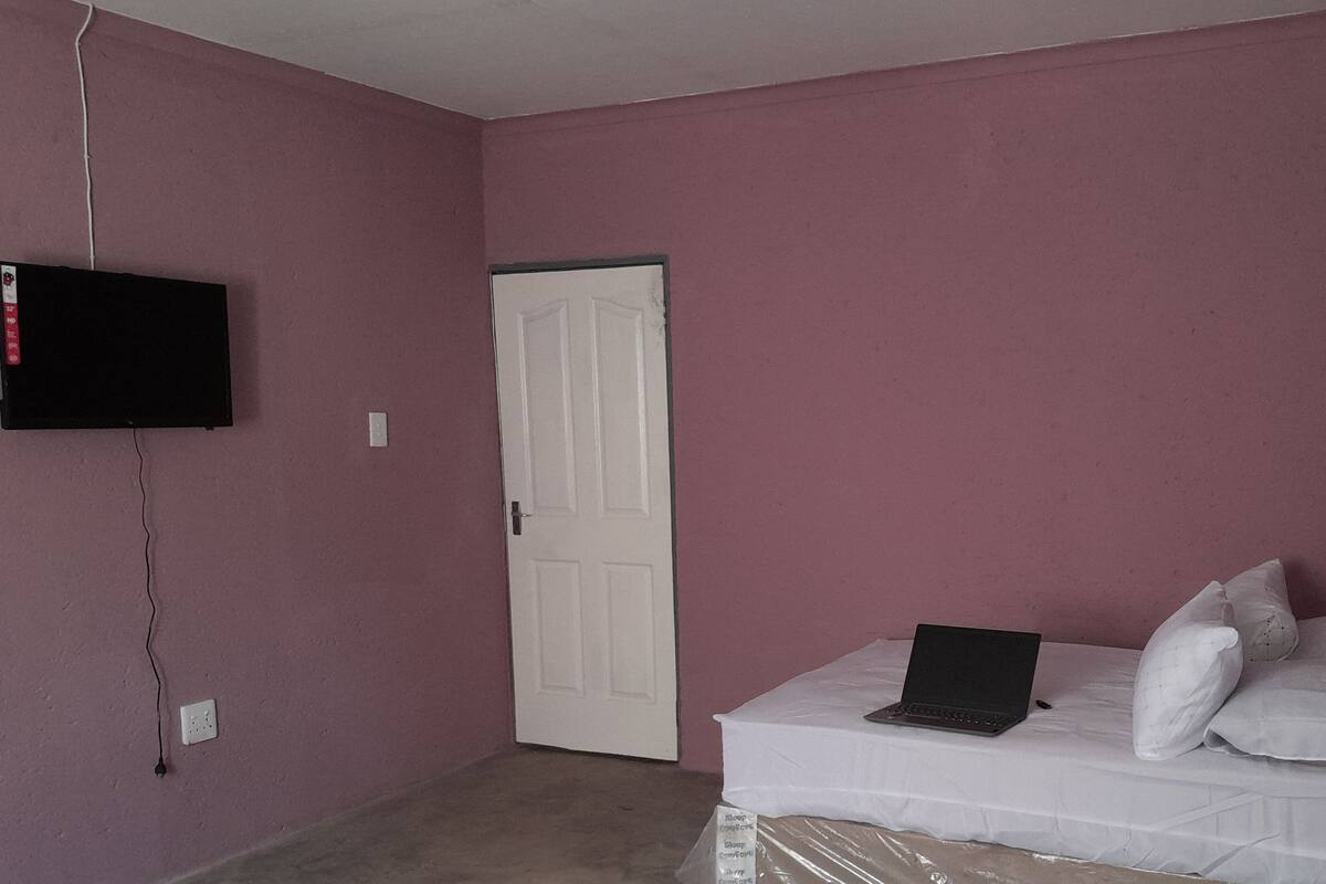 A bedroom with a white bed, a laptop, a television on the wall, and a closed door.