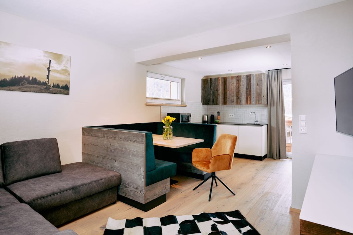 A modern living room with a sofa, a dining table with chairs, and a kitchen area with wooden cabinets.