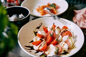 A plate of Caprese salad with tomatoes, mozzarella, and basil, served on a white plate.