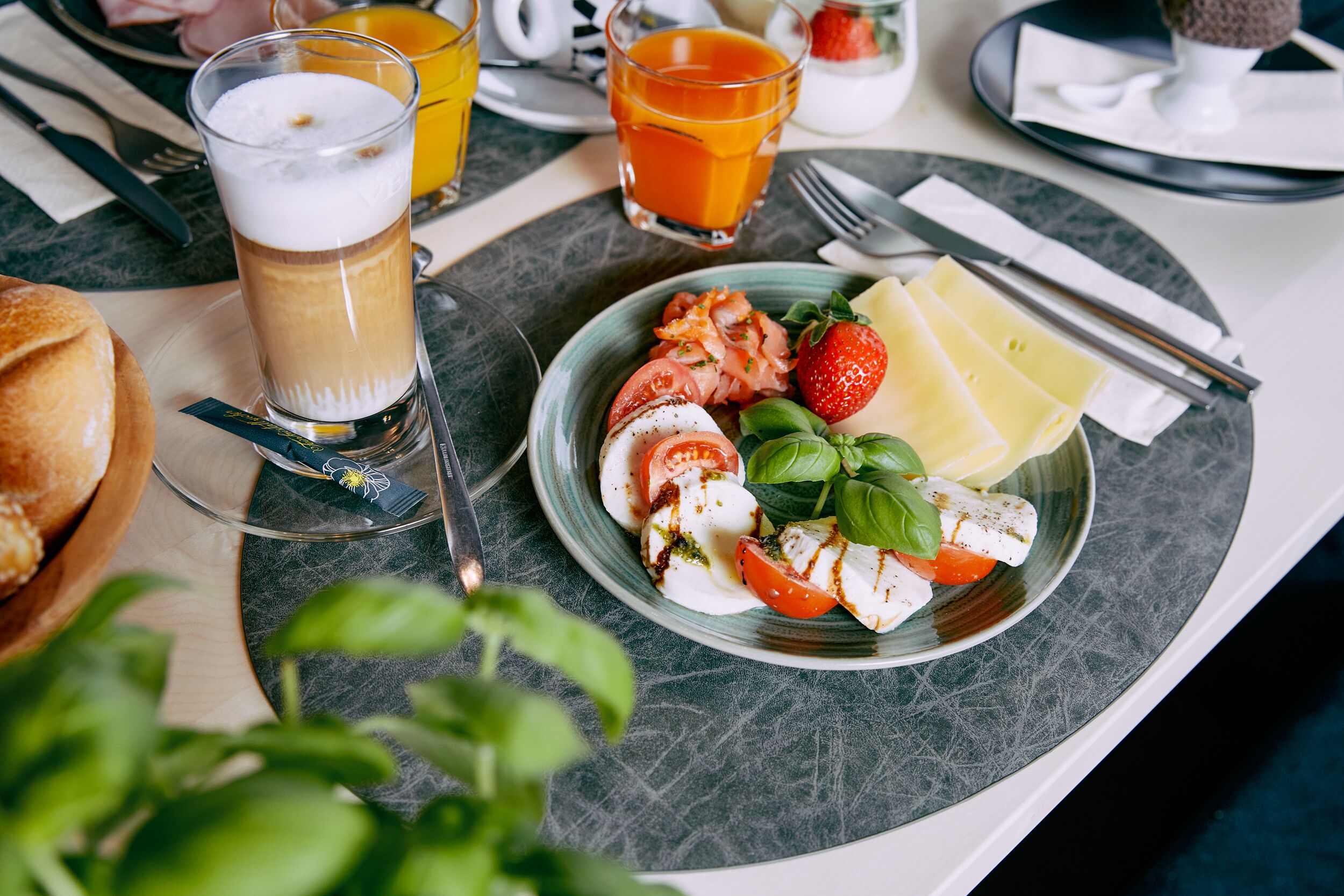 A breakfast setting with a plate of Caprese salad, a glass of orange juice, and a glass of beer.