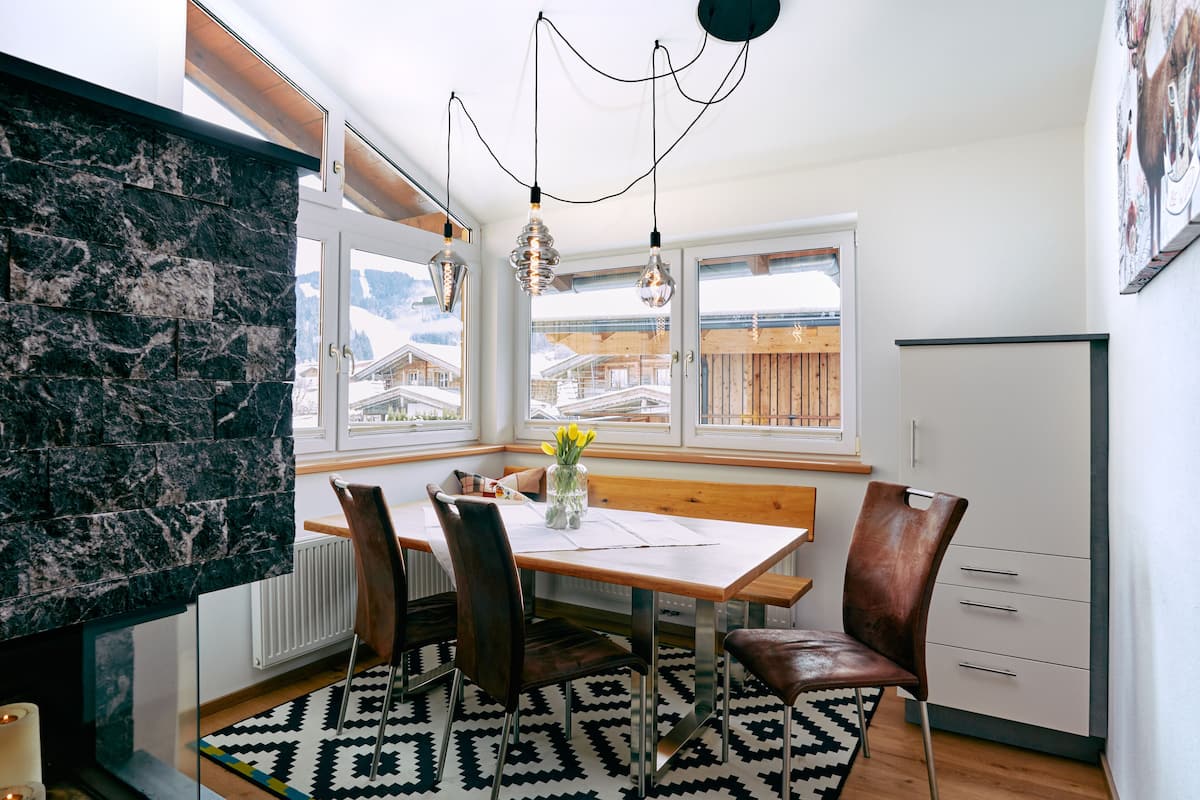 A modern kitchen with a dining table, chairs, and a view of snow-covered houses through large windows.