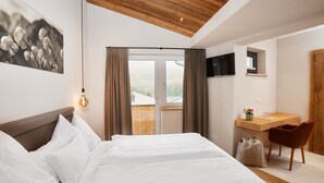 A hotel room with a bed, a desk with a chair, a TV, and a window with curtains. - Home Suite Home (Fieberbrunn)