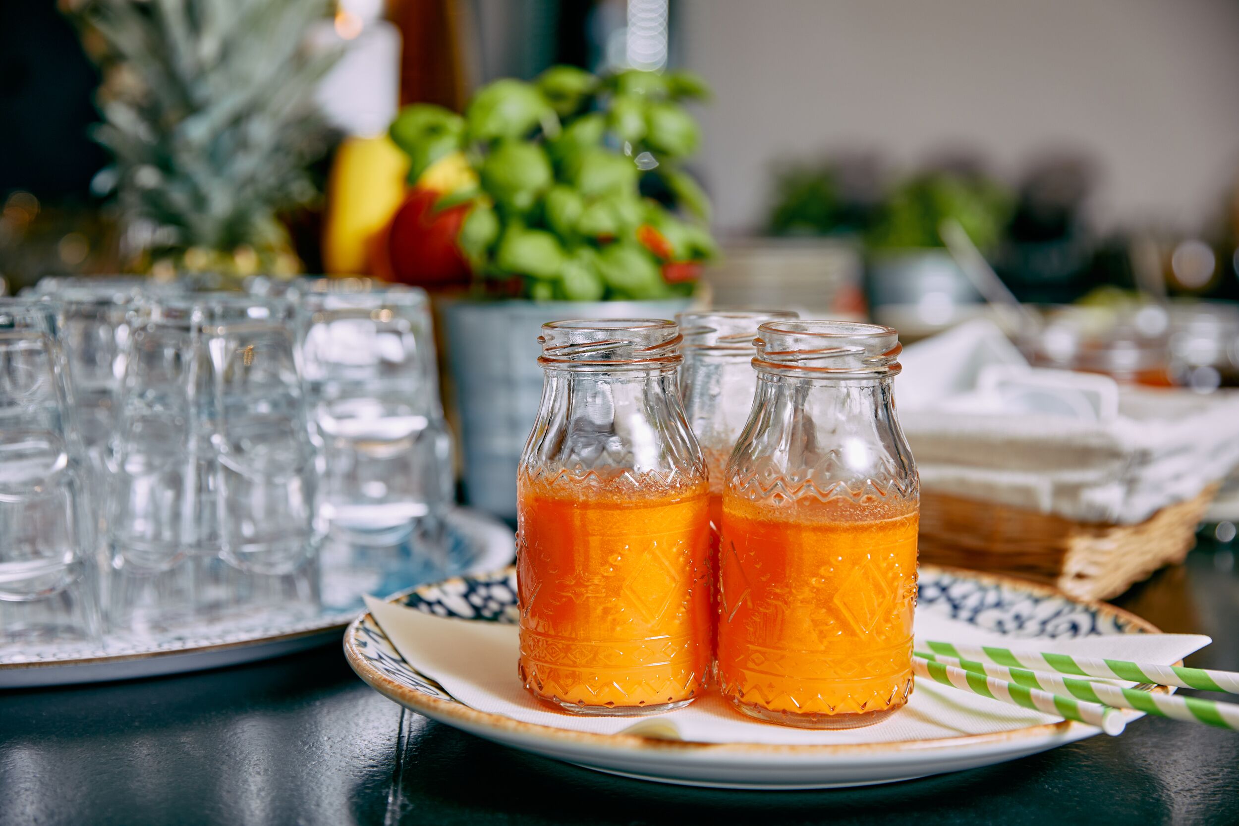 A table with two glass bottles of orange beverage, a plate with a checkered napkin, and a decorative pineapple in the background.