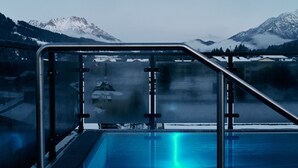 A pool area with a glass railing, a blue pool, and a view of snow-capped mountains in the background. - Home Suite Home (Fieberbrunn)