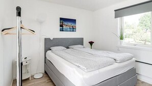 Una camera da letto moderna con un letto, un comodino, una lampada da terra, una finestra con vista e un quadro appeso al muro.