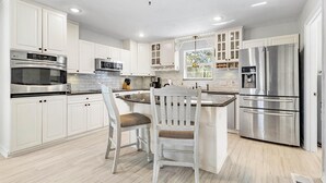 Une cuisine moderne avec des meubles blancs, des appareils en acier inoxydable et un îlot central doté d’un tabouret.