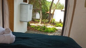 A room with a bed, a towel, and a view of a garden with trees and a white building. - eco-Hotel Carigua (Barichara)