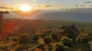 A rural landscape with thatched-roof huts, a stone pathway, and a view of distant hills. - eco-Hotel Carigua (Barichara)