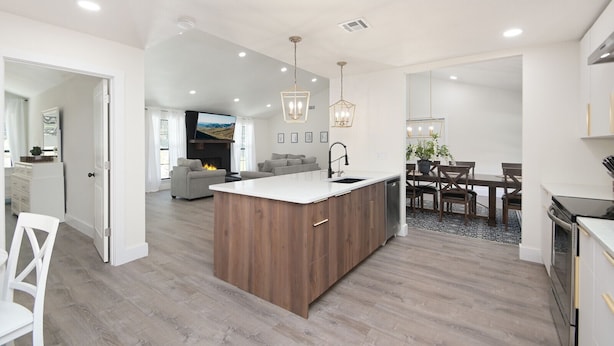 A modern kitchen with a central island, a dining area with a table and chairs, and a living room with a sofa and fireplace.
