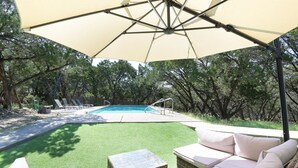 A backyard with a swimming pool, green lawn, and outdoor furniture.