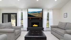 A living room with a fireplace, two sofas, and a large TV screen.