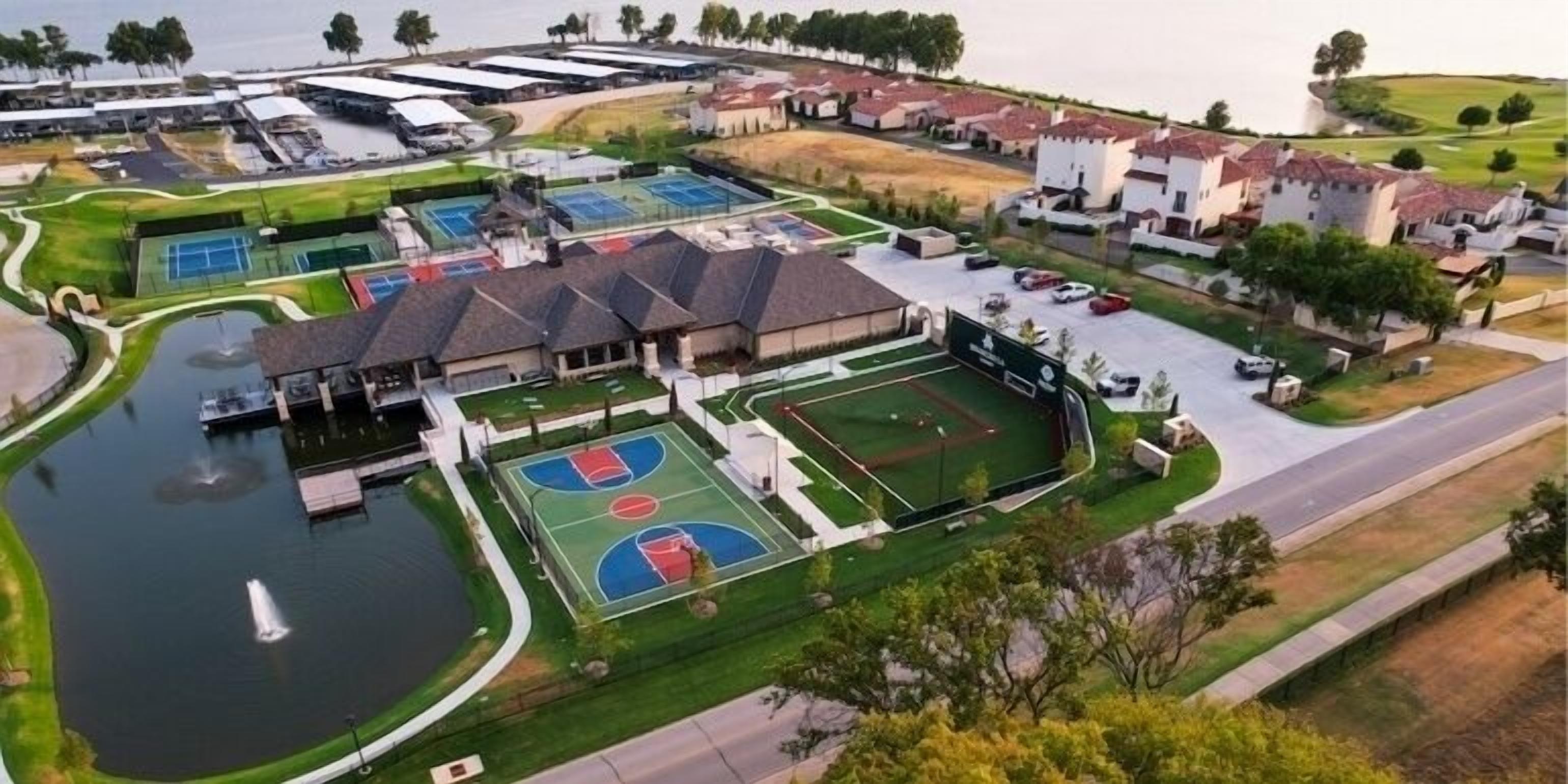 Ein Luftbild eines Wohngebiets mit mehreren Tennisplätzen, einem Schwimmbad und Häusern mit roten Ziegeldächern.